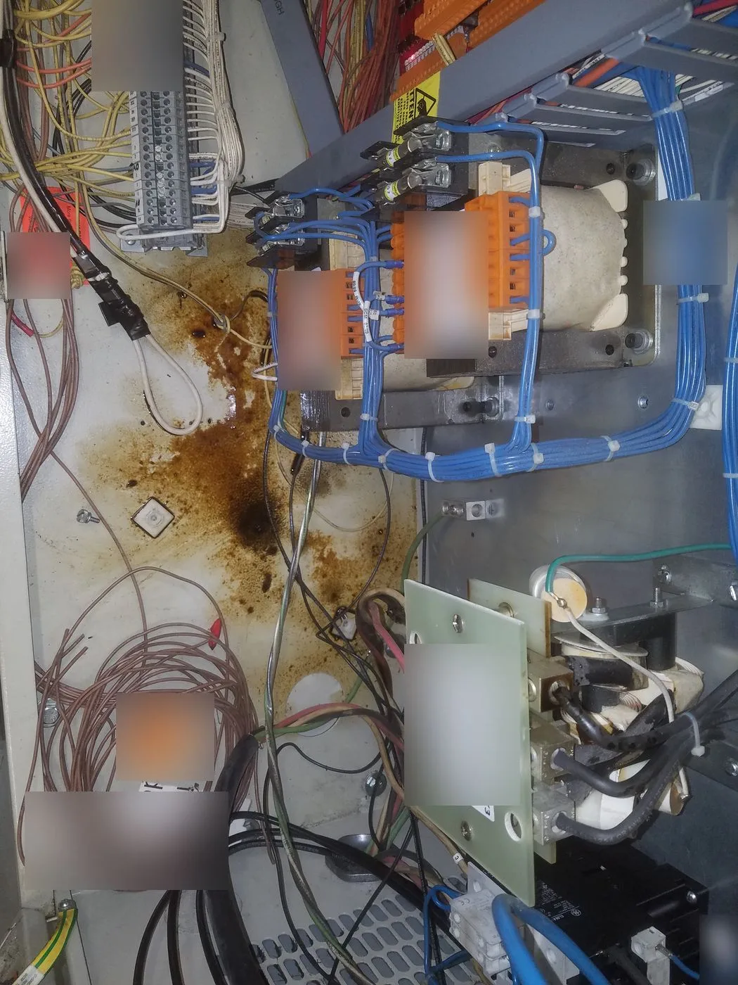Inside an elevator controller cabinet showing oil spreading across the backplane below the transformers